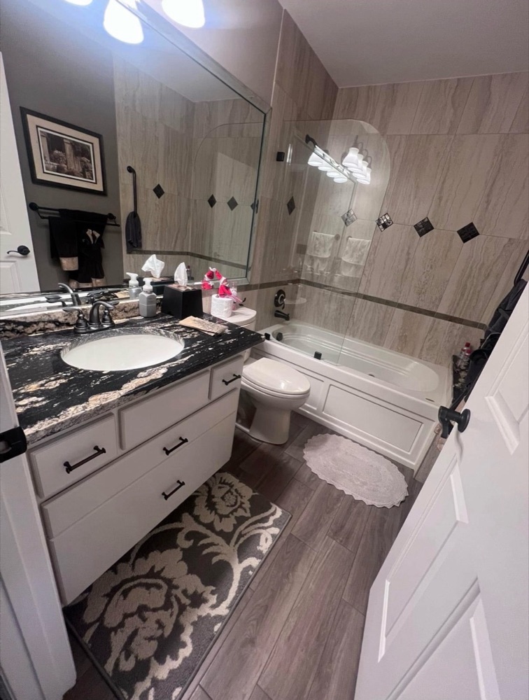 A freshly cleaned bathroom with a granite vanity, tiled tub surround and spotless floors